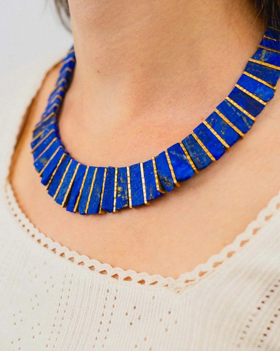 Blue lapis lazuli tab necklace with gold accents worn on a woman's neck