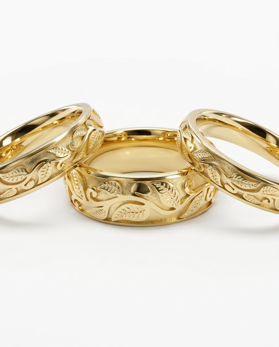 Three gold wedding rings featuring an intricate embossed leaf motif on a textured background.