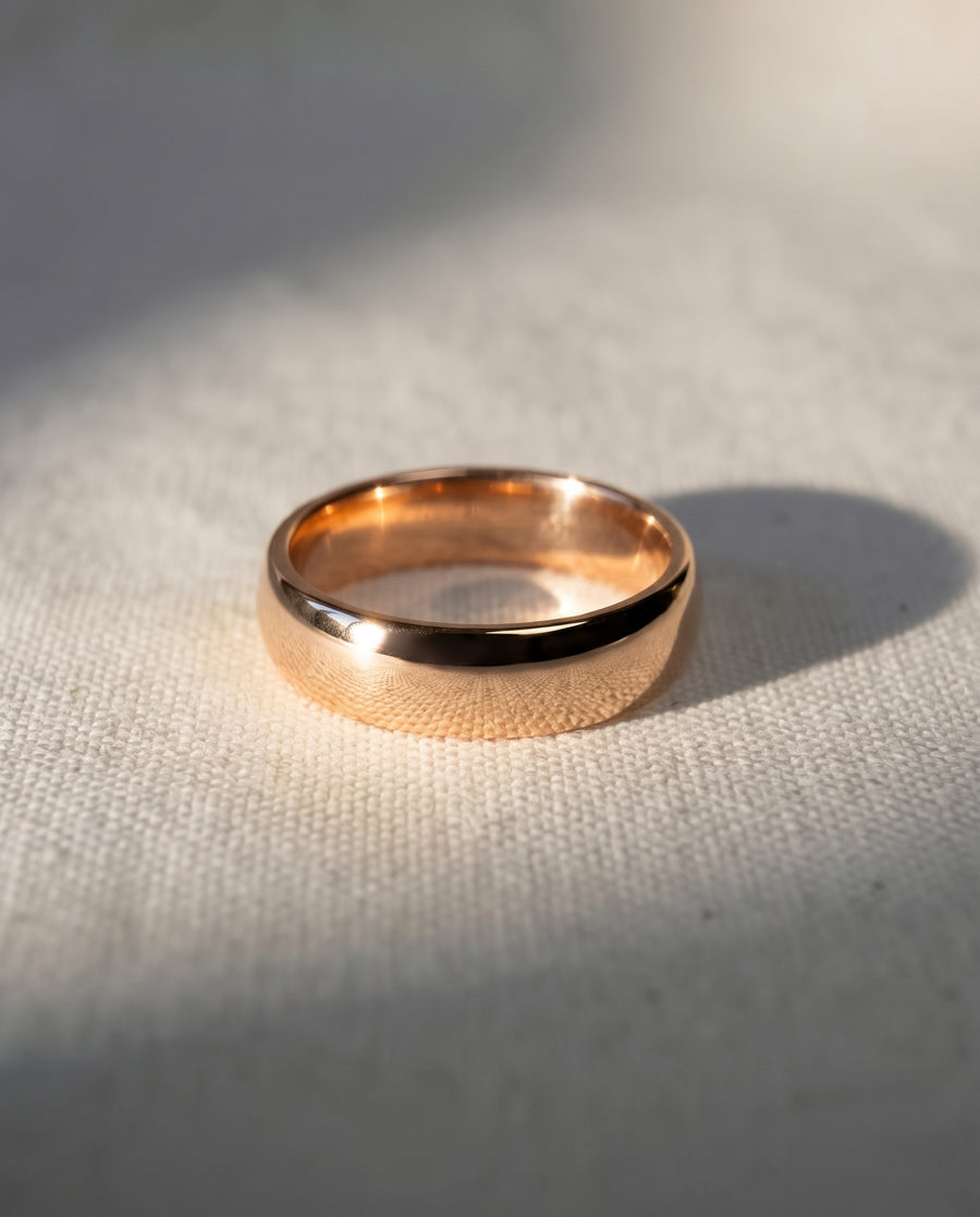 4mm polished 9ct rose gold low court wedding ring with a smooth, rounded profile on a textured surface.