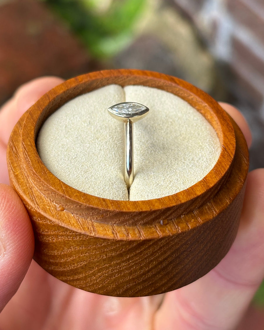 Marquise cut diamond engagement ring in a gold bezel setting inside a round wooden box.