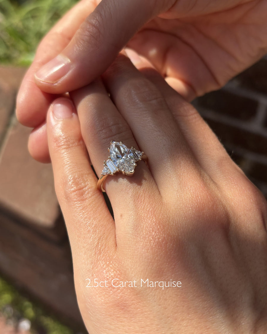 Gold engagement ring with a marquise cut diamond and claw side stones.