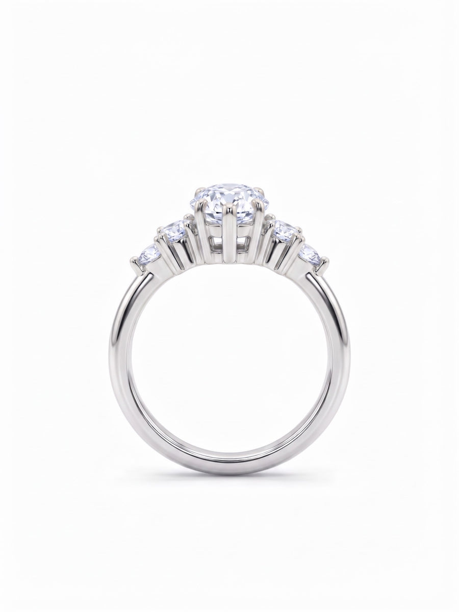 Silver engagement ring with a central round diamond and smaller side stones in a claw setting.