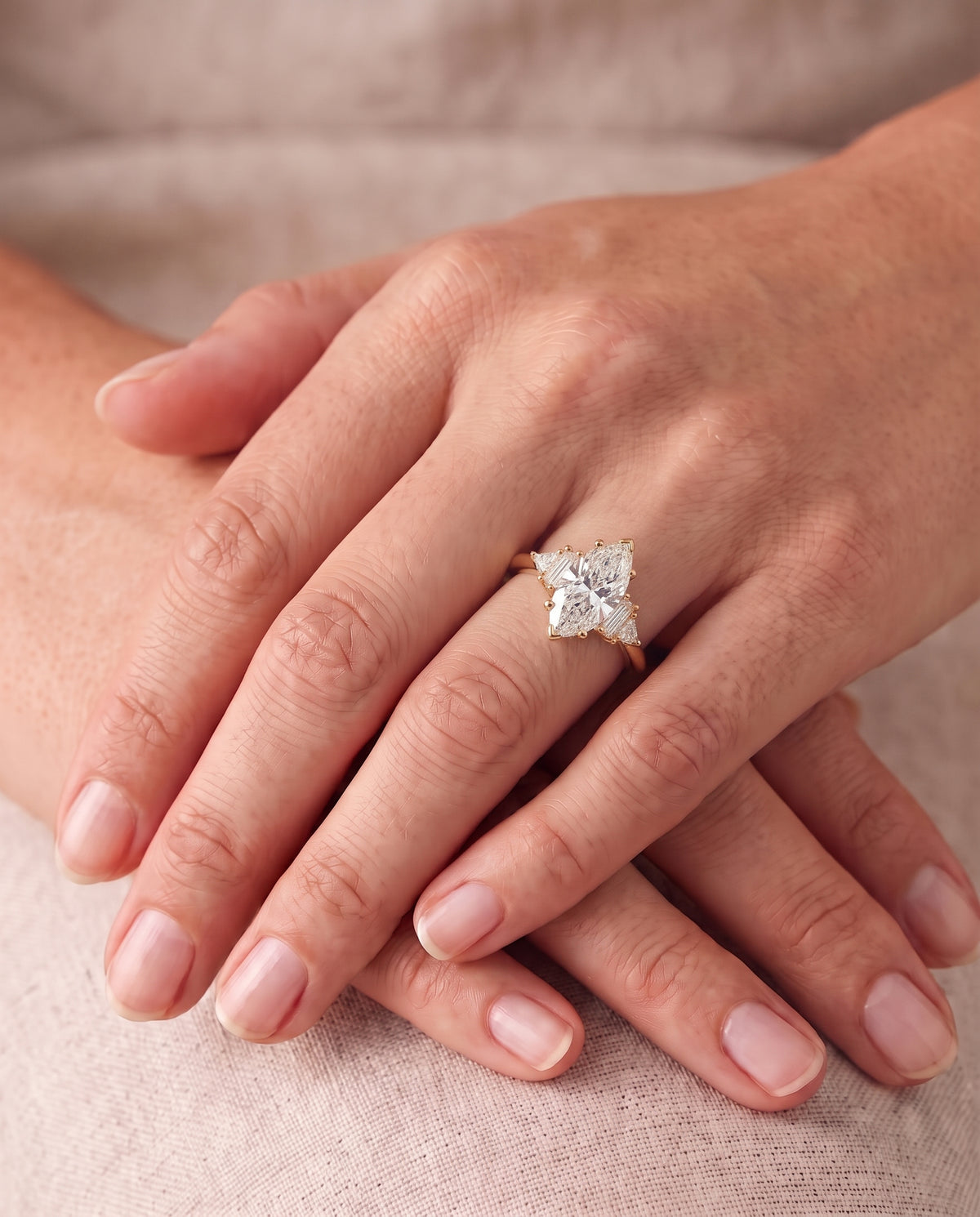 Gold engagement ring with a marquise cut center diamond and baguette side stones on a finger.