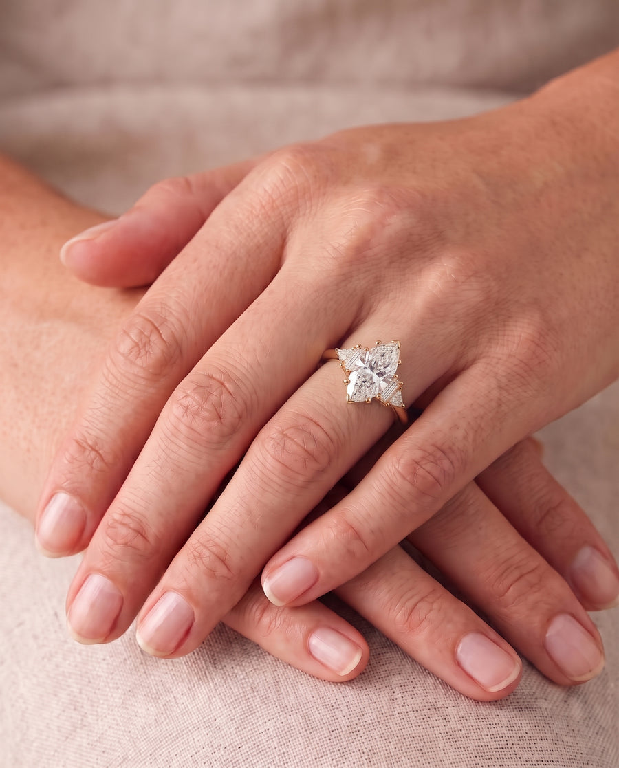 Gold engagement ring with a marquise cut center diamond and small side stones on a finger.