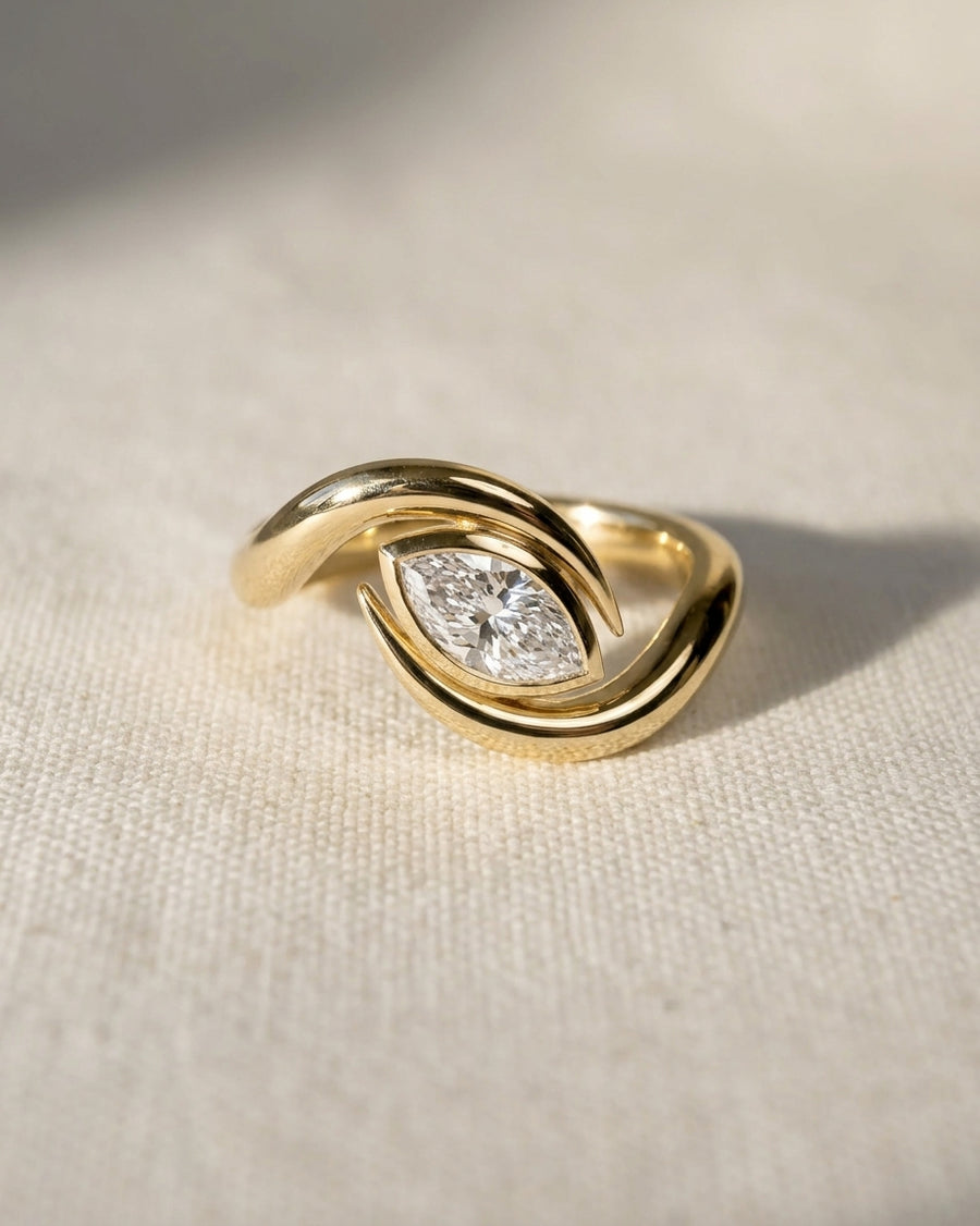 18ct yellow gold engagement ring featuring a marquise cut diamond set in a curved, spiky bypass band.