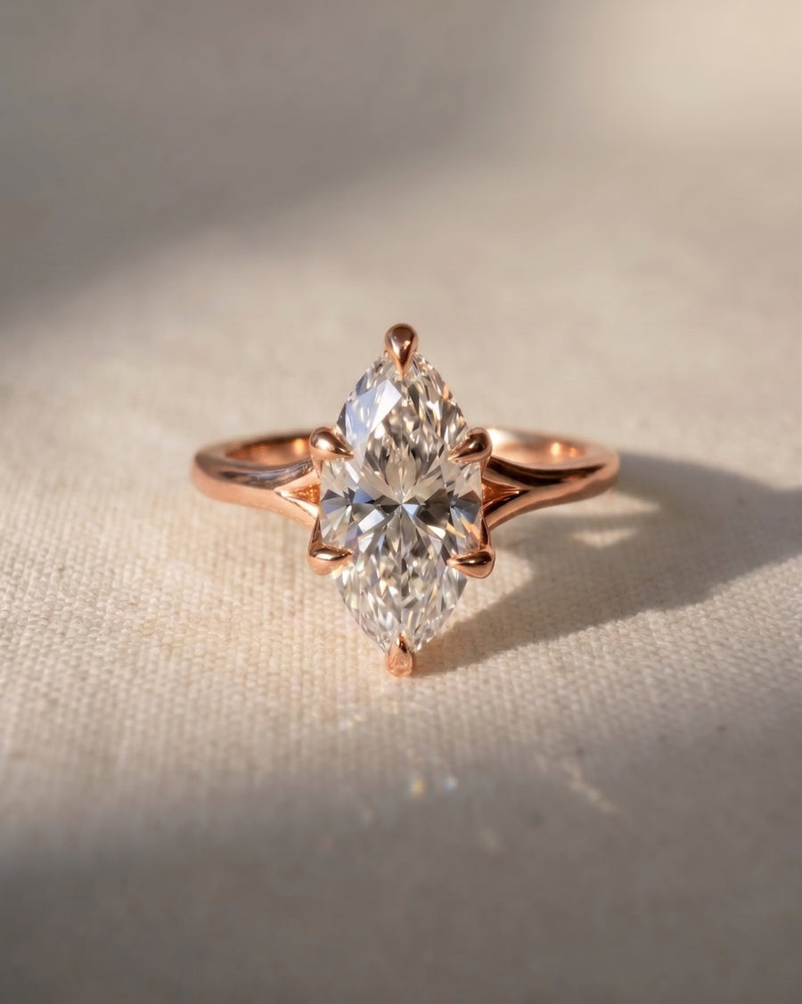 Marquise cut diamond engagement ring in 18ct rose gold with a tulip claw setting on a textured surface.