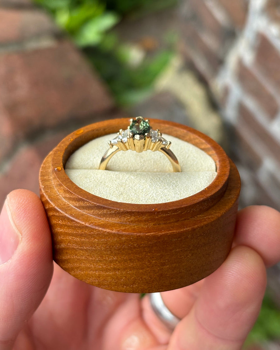 Marquise cut green sapphire engagement ring with diamond side stones in a gold setting inside a wooden box.