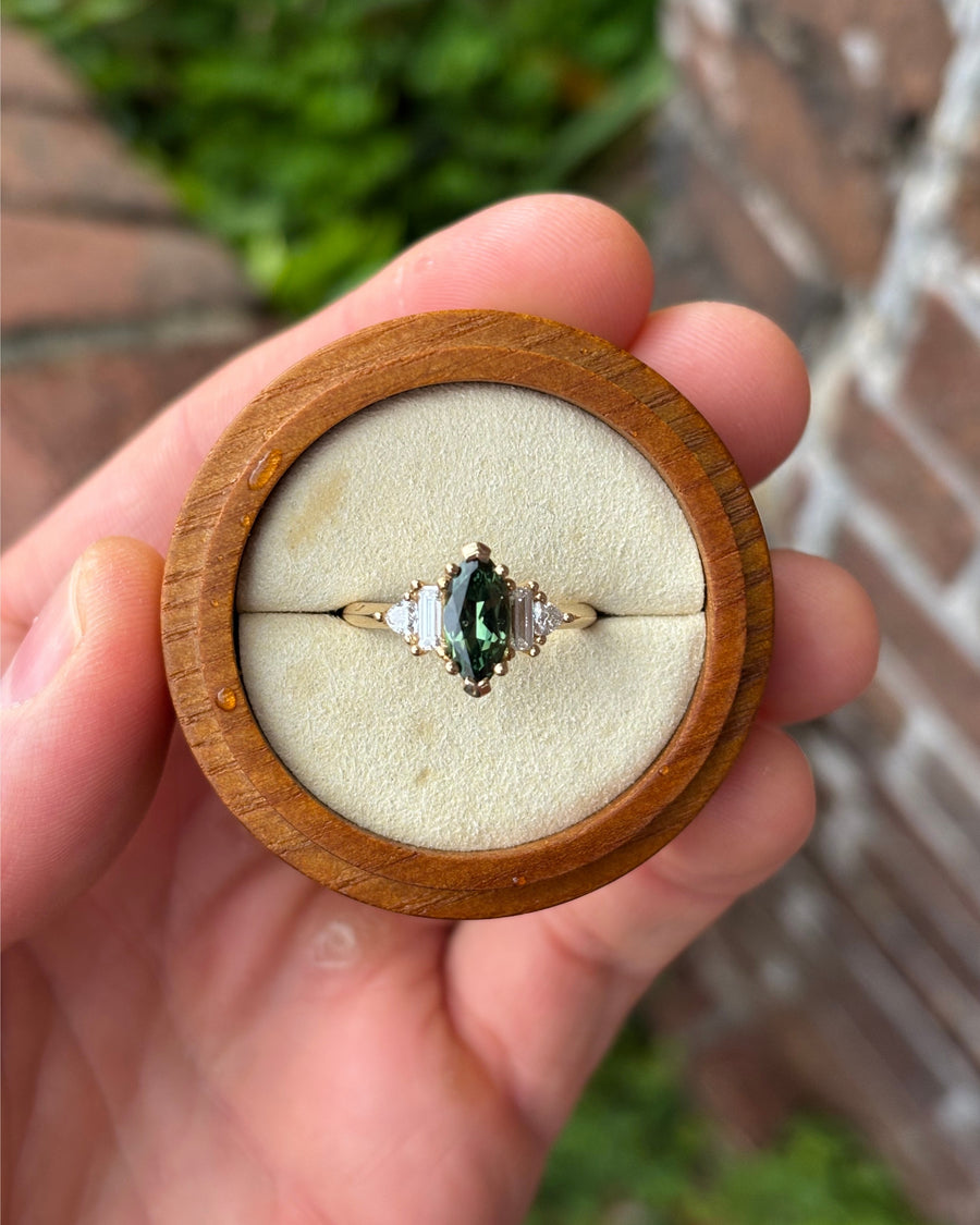 Marquise cut green sapphire engagement ring with side stones in 9ct yellow gold, held in a wooden box.