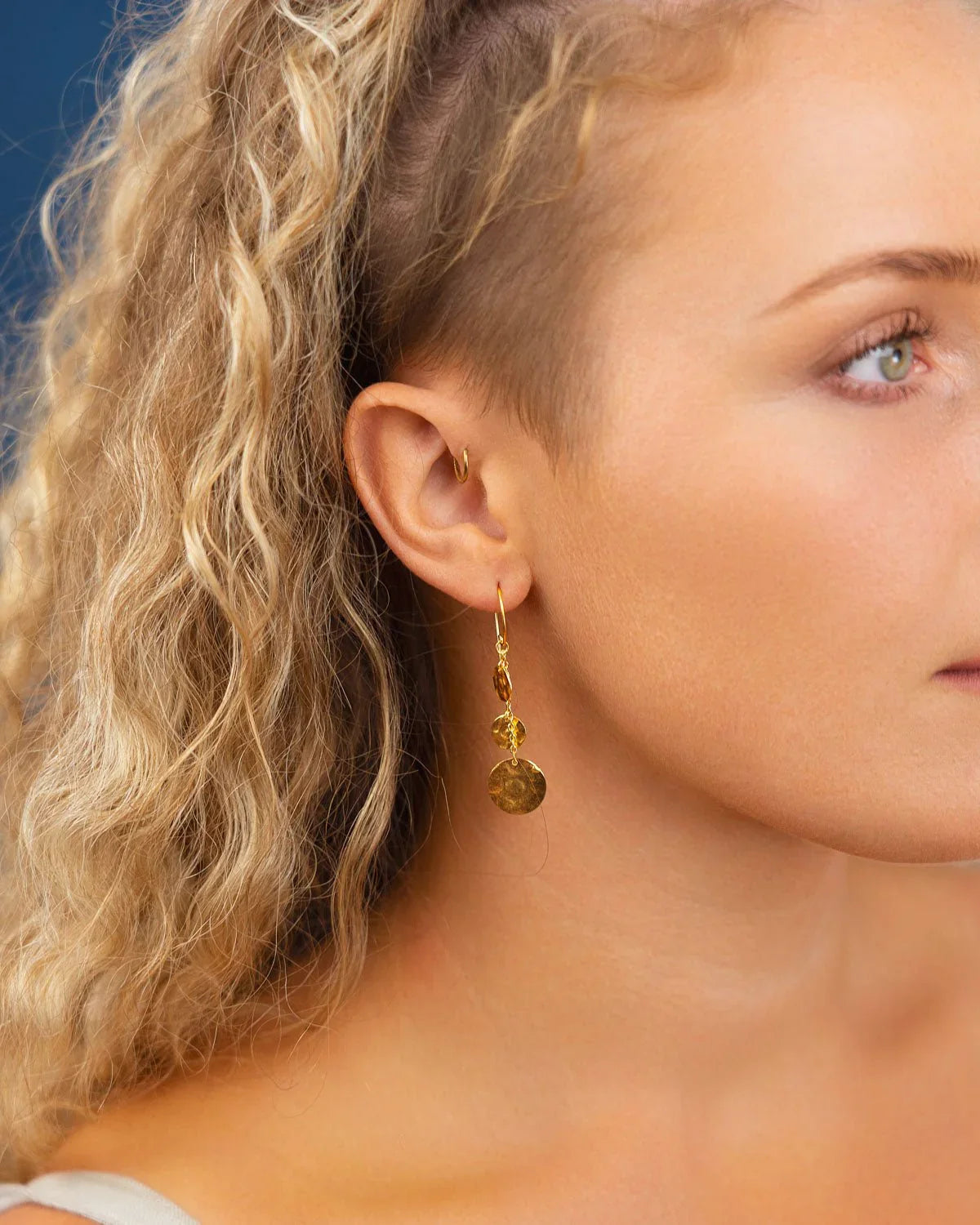 Woman wearing hammered gold disc dangly earrings with organic texture
