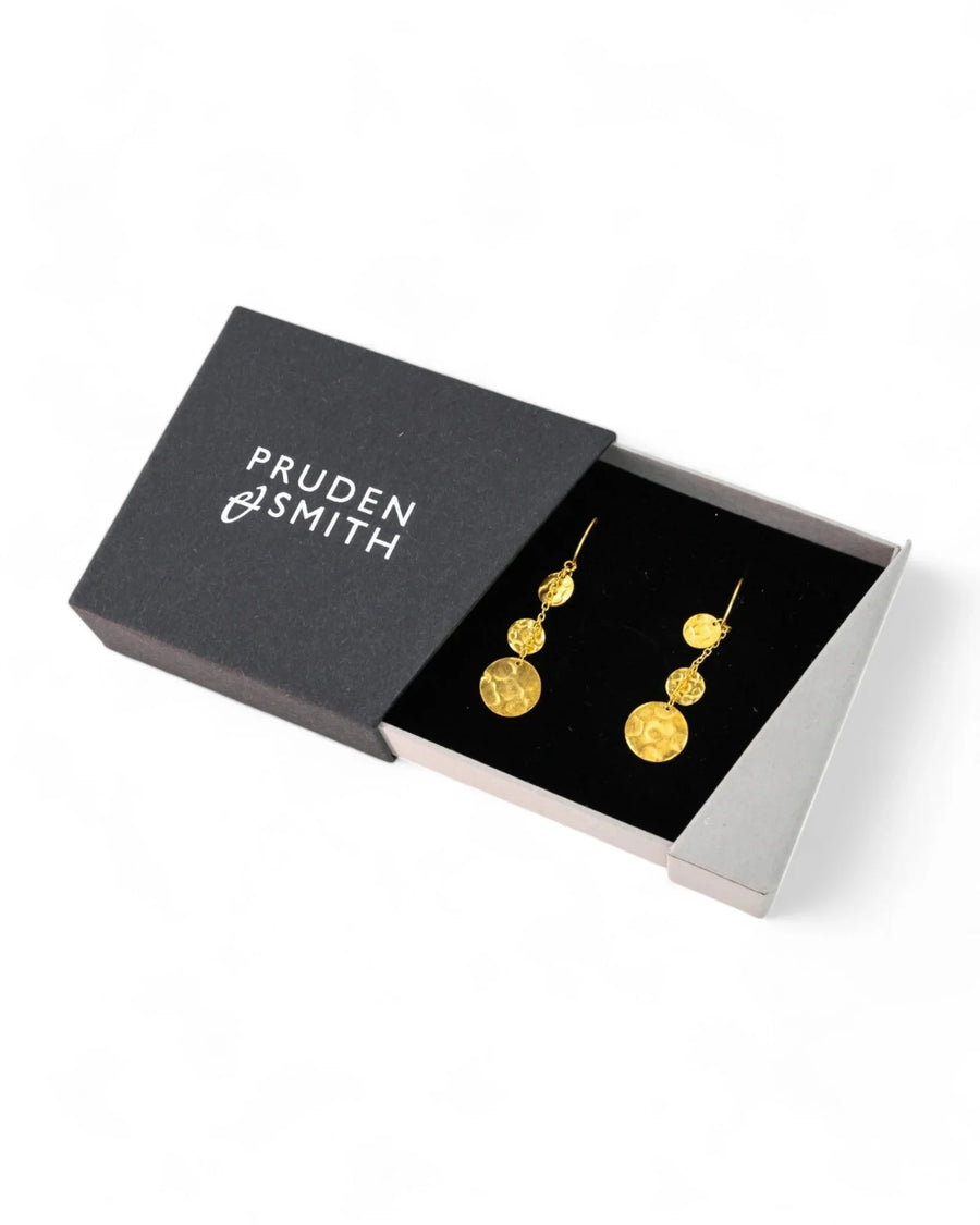 Dangly gold hammered disc earrings in a black jewelry box on a white background