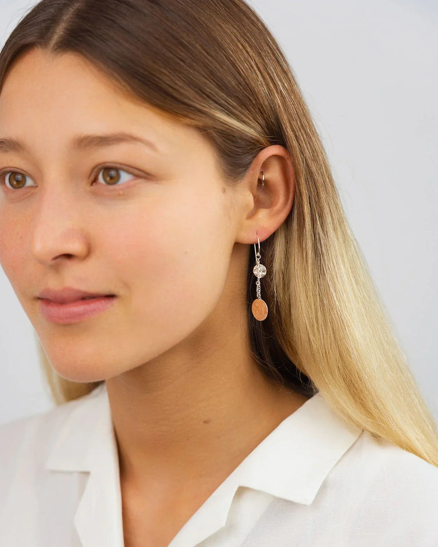 Woman wearing hammered disc dangly earrings with silver and gold tones, minimal style