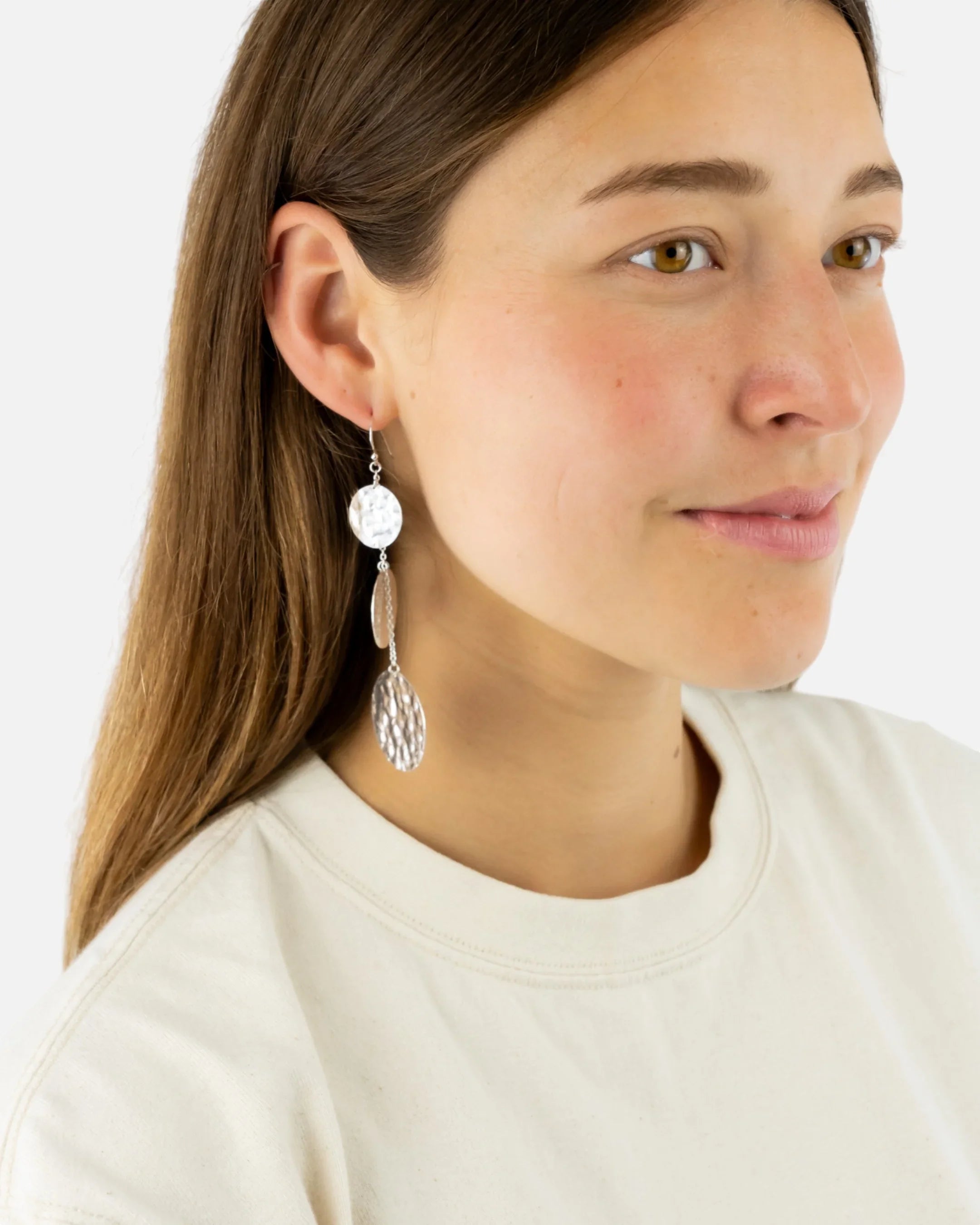 Woman wearing handmade silver drop earrings with organic, hammered texture, luxury jewellery