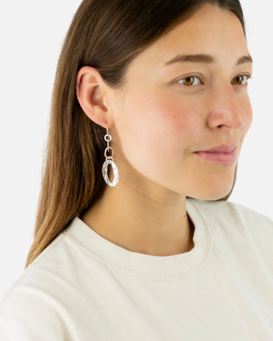 Woman wearing handmade silver oval drop earrings with hammered texture, luxury jewellery
