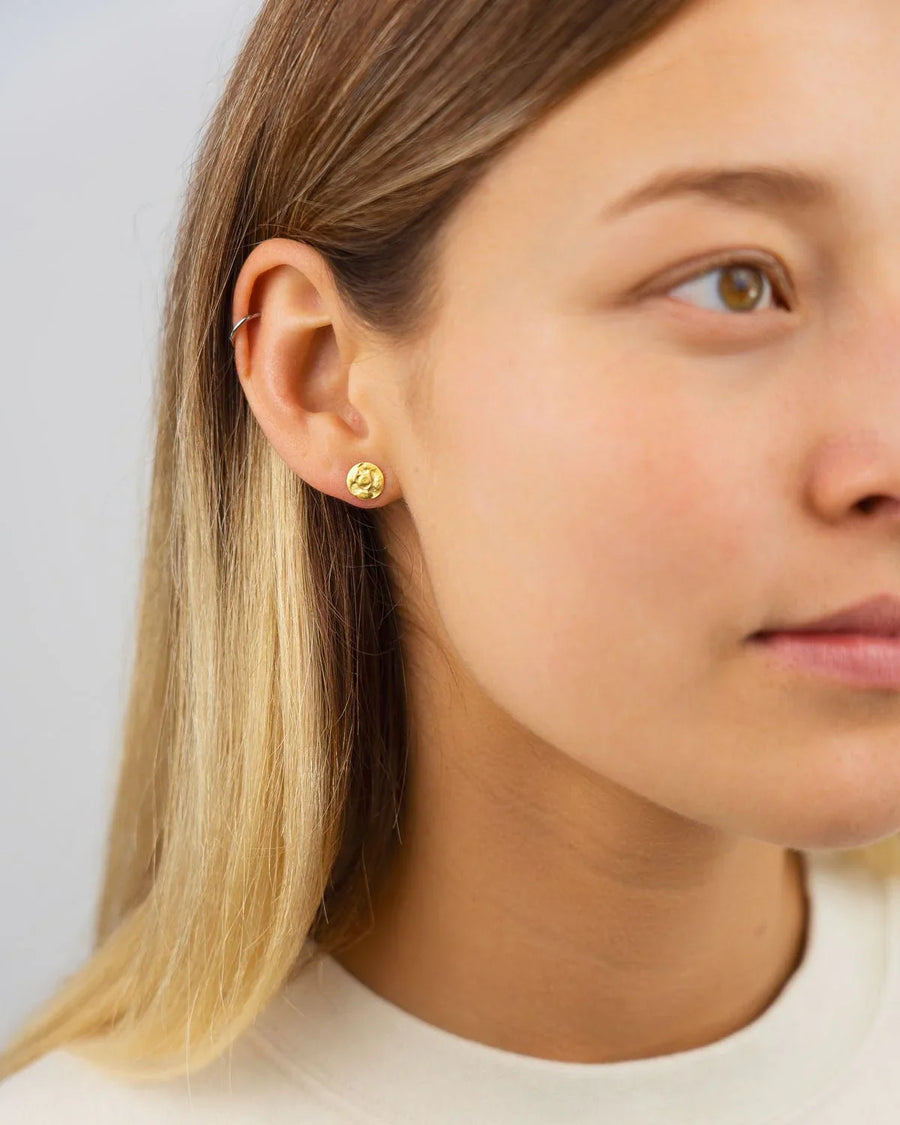 Gold hammered stud earrings on a woman's ear.
