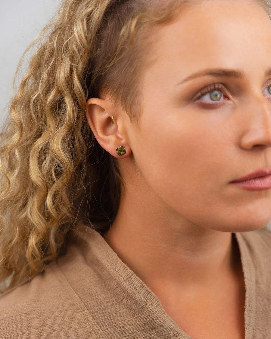 Hammered gold stud earrings with a green gemstone on a woman's ear.