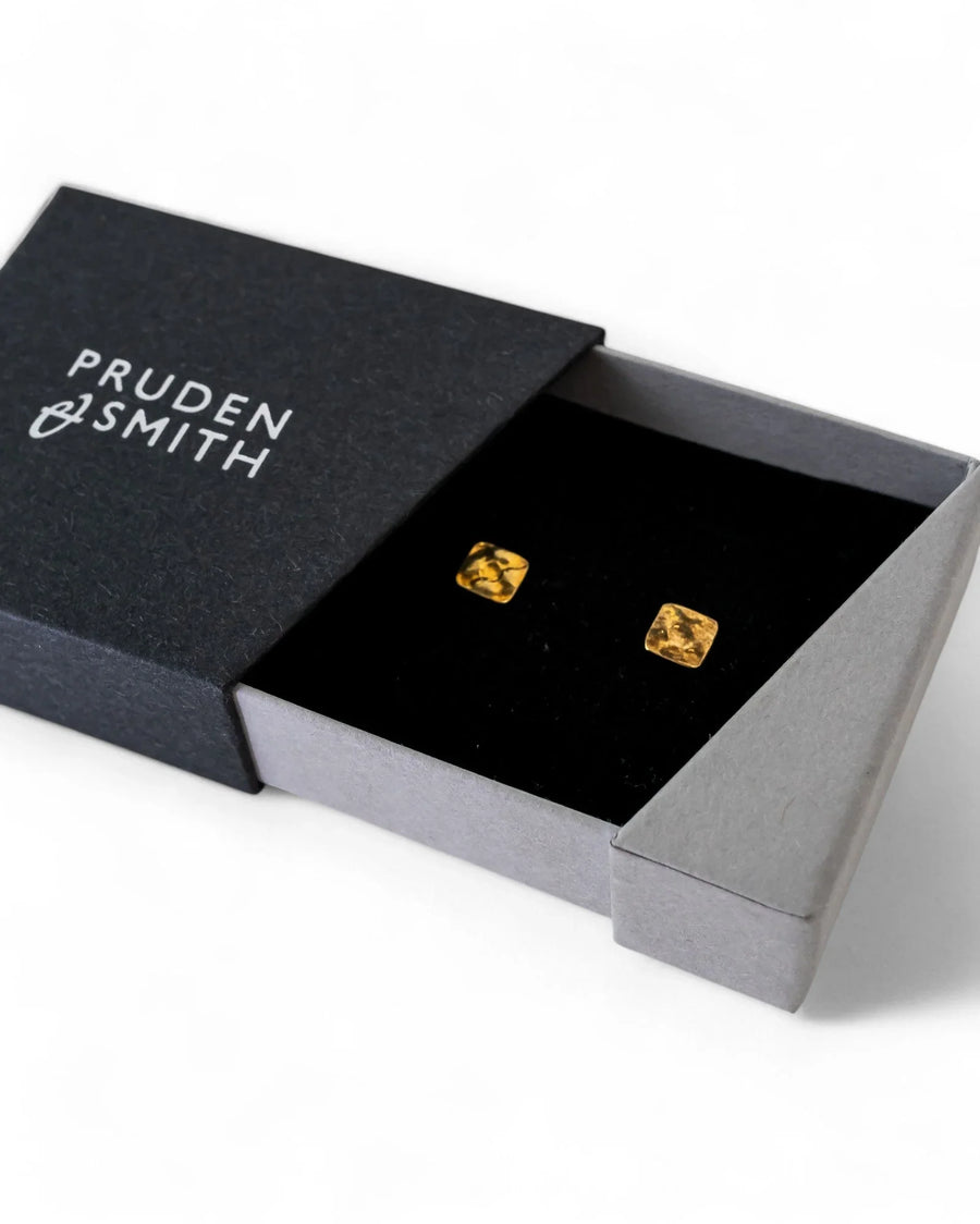 Gold hammered stud earrings in a black velvet-lined box.