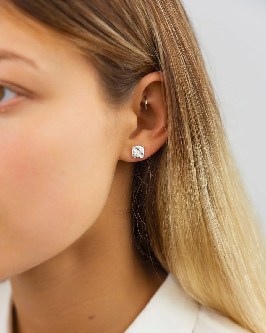 Silver hammered square stud earring on an ear.