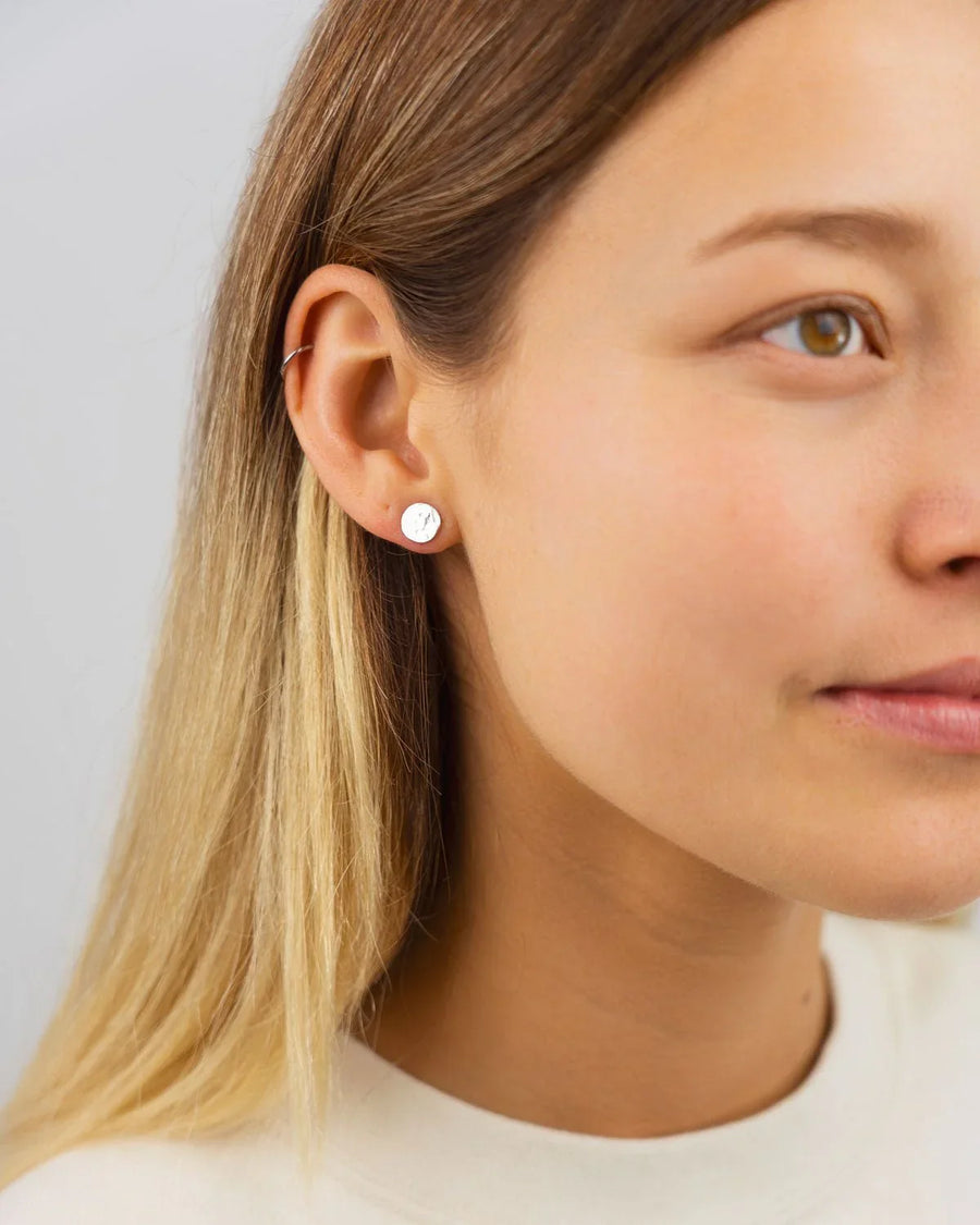 Silver round hammered stud earring on an ear.