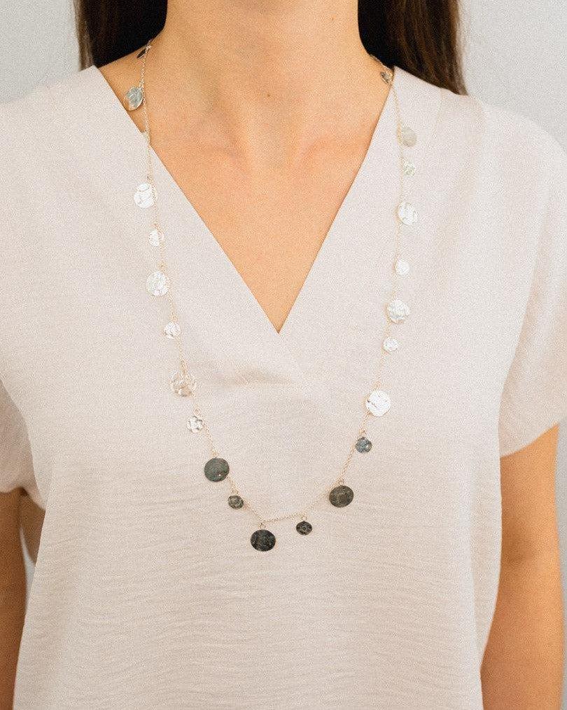 Handmade silver disc necklace with textured organic pendants on model in white top