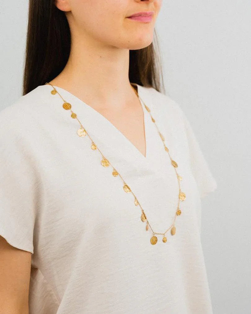 Delicate gold coin necklace with organic shapes worn over a simple cream top
