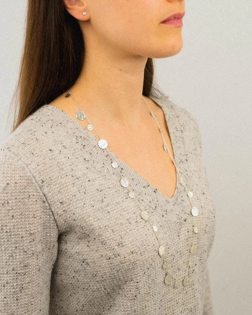Long silver disc necklace with organic hammered texture on woman in grey sweater
