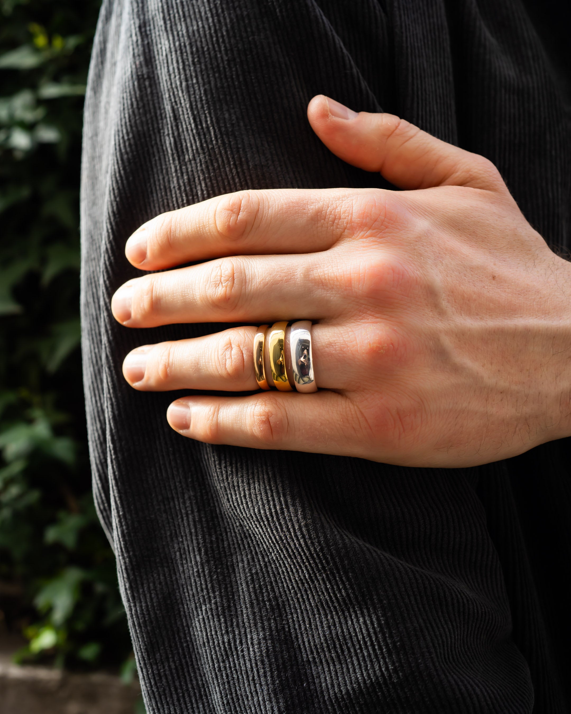 Hand wearing three chunky gold and silver wedding rings against a dark textured jacket