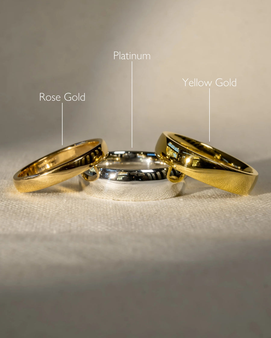 Three polished low court wedding rings: rose gold, platinum, and yellow gold.