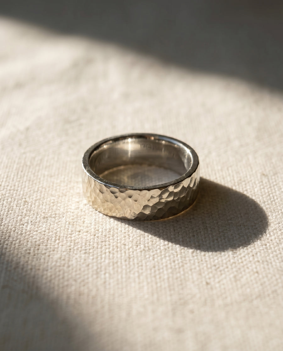 Men's flat hammered silver wedding ring on a light fabric surface.