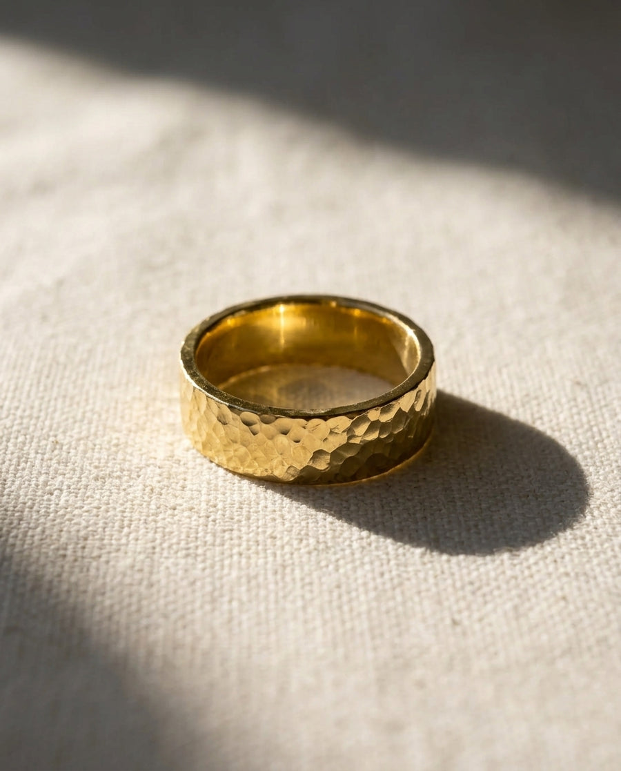 Gold flat hammered wedding ring on a light fabric surface.