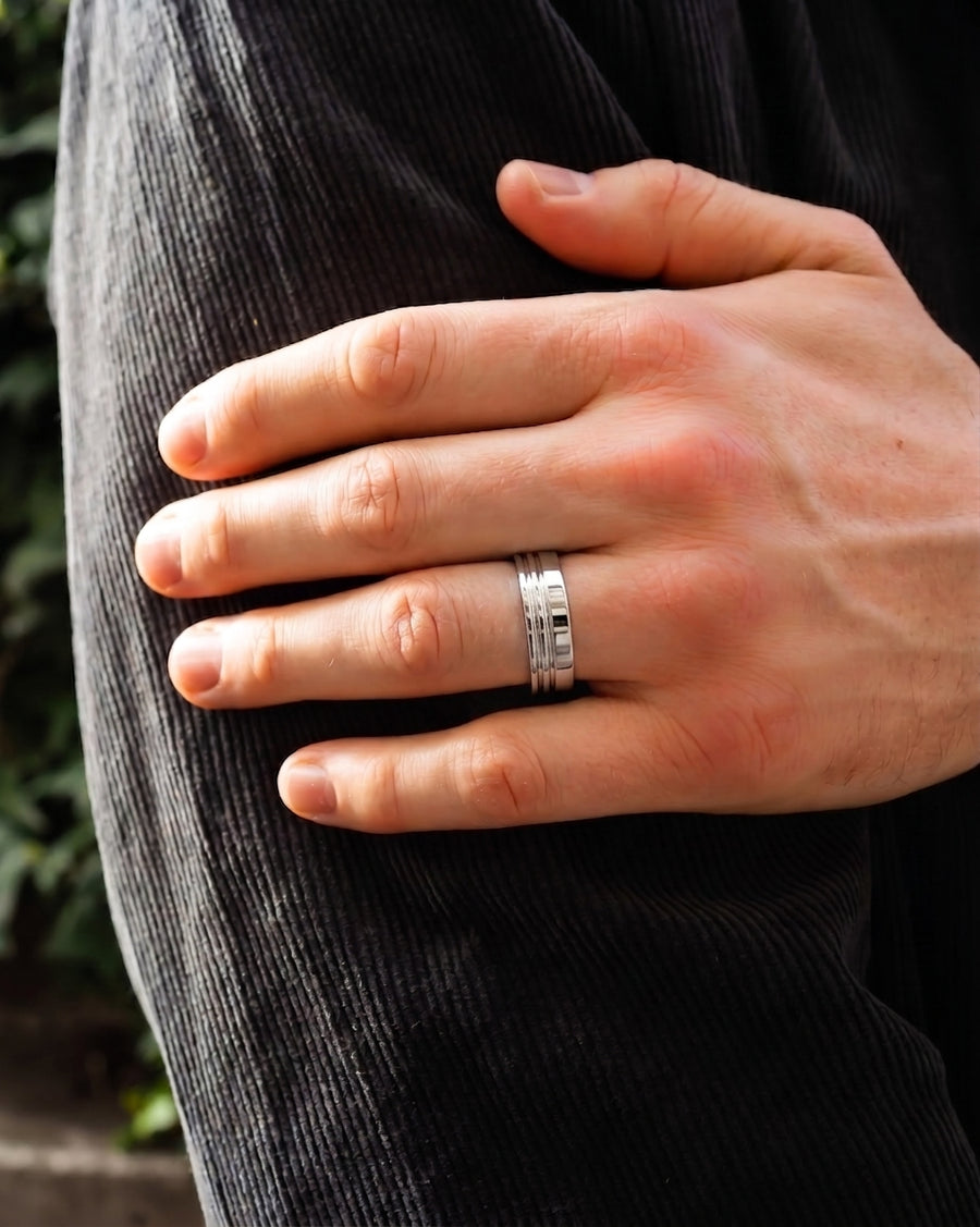 Men's flat silver wedding ring with three engraved lines on a hand.