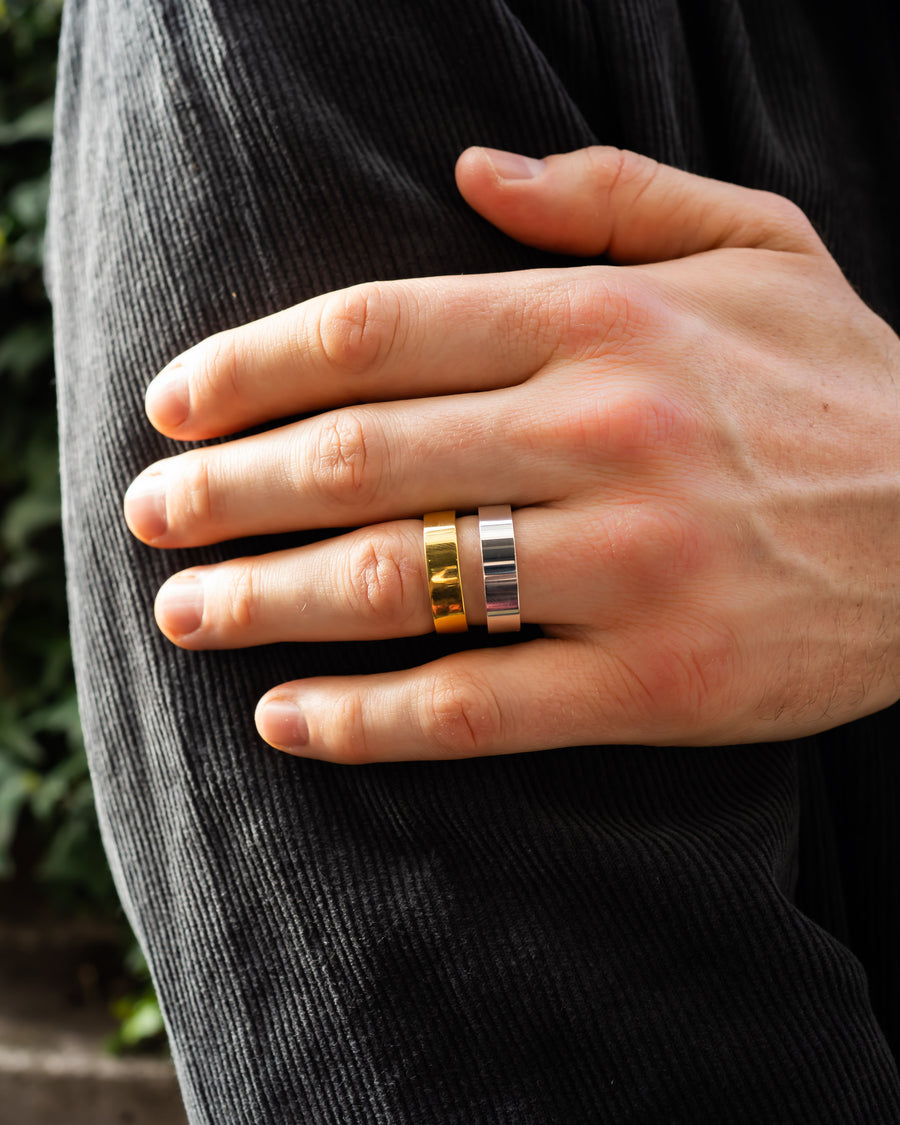 A man's hand wearing a gold and a silver flat wedding ring.
