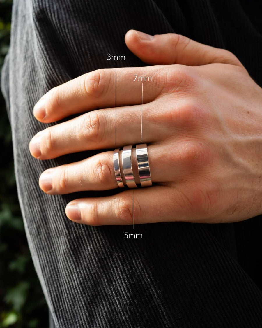 Men's flat silver wedding rings in 3mm, 5mm, and 7mm widths on a hand.