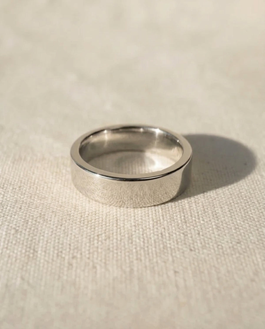 Polished silver-tone flat wedding ring with a smooth, minimalist band design on a textured fabric surface.