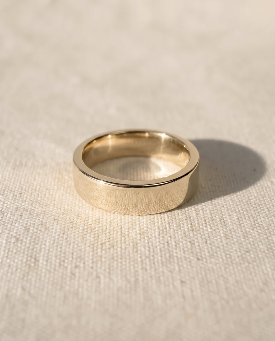 Polished yellow gold wedding ring with a flat band design resting on a textured fabric surface.