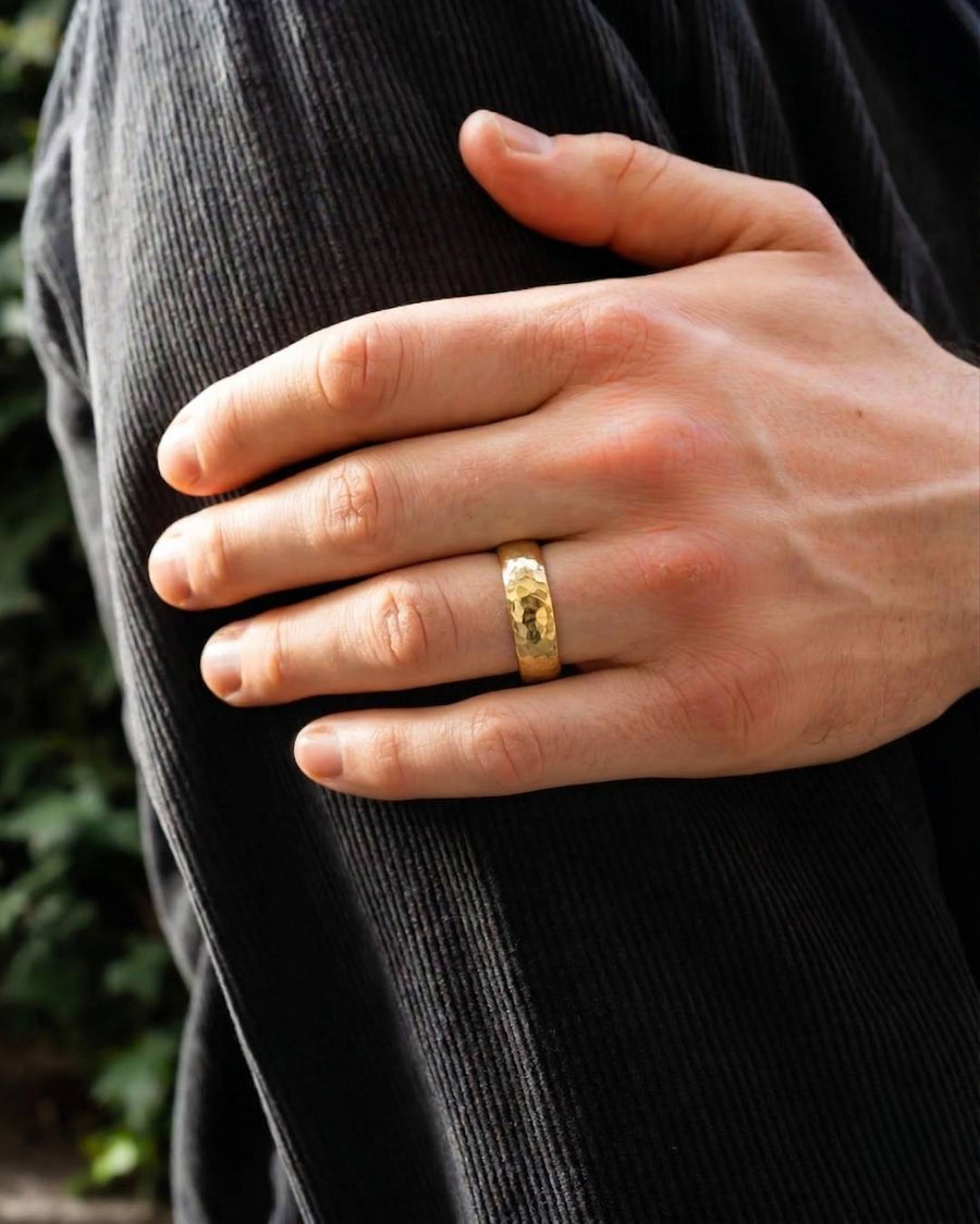 Gold hammered court wedding ring worn on a man's finger.