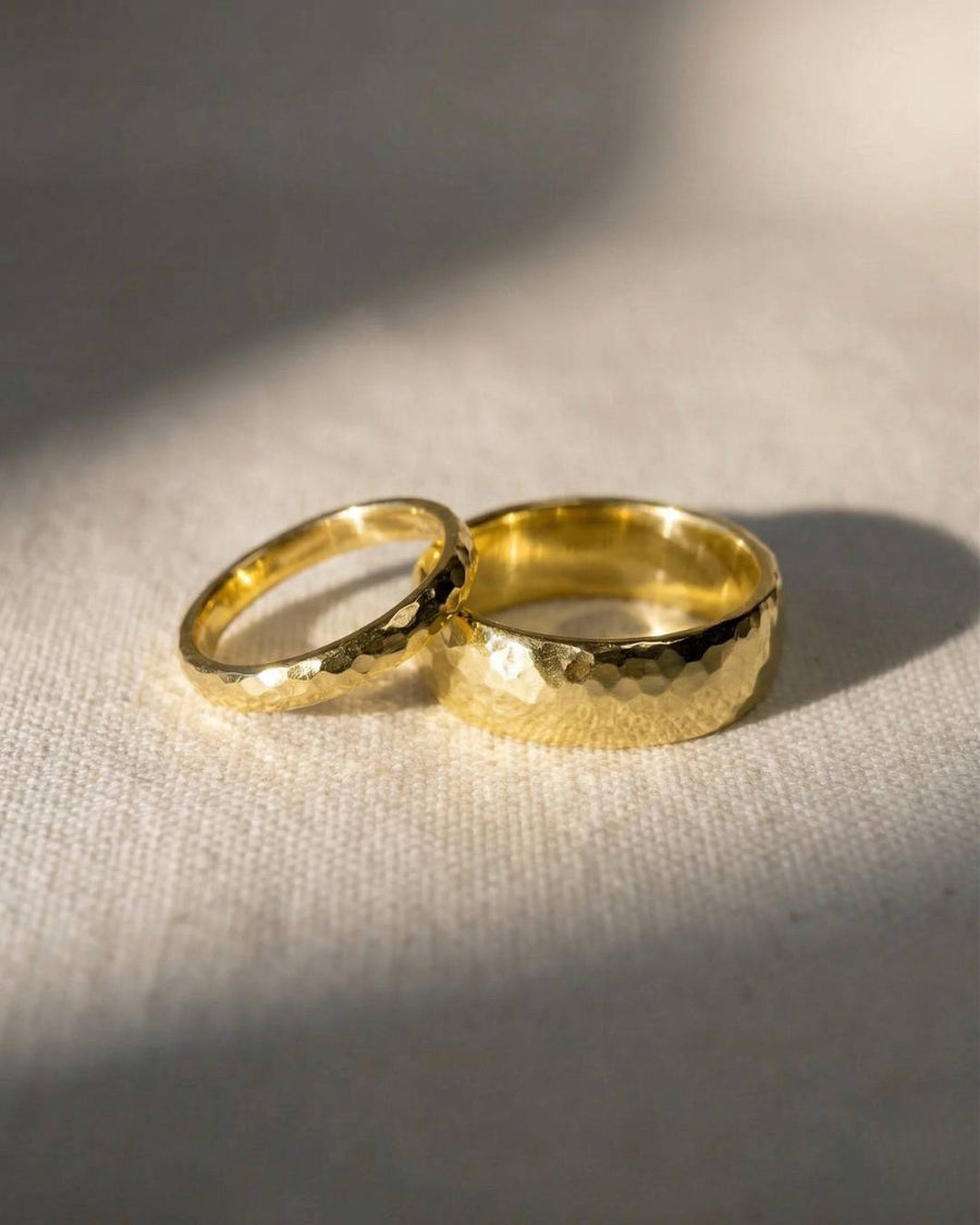 Two gold wedding rings with a hammered texture resting on a textured fabric surface.