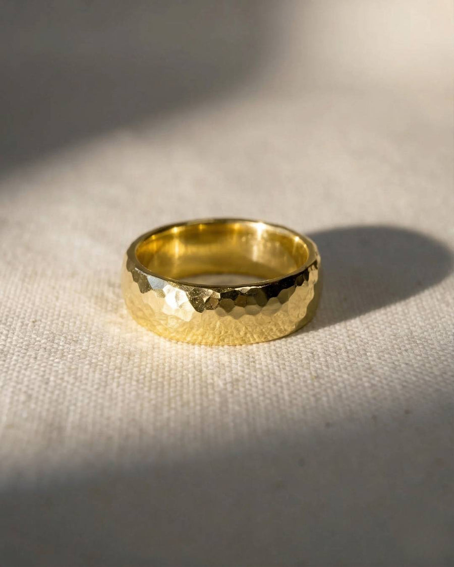 Gold wedding ring with a hammered texture and court shape resting on a textured fabric surface.