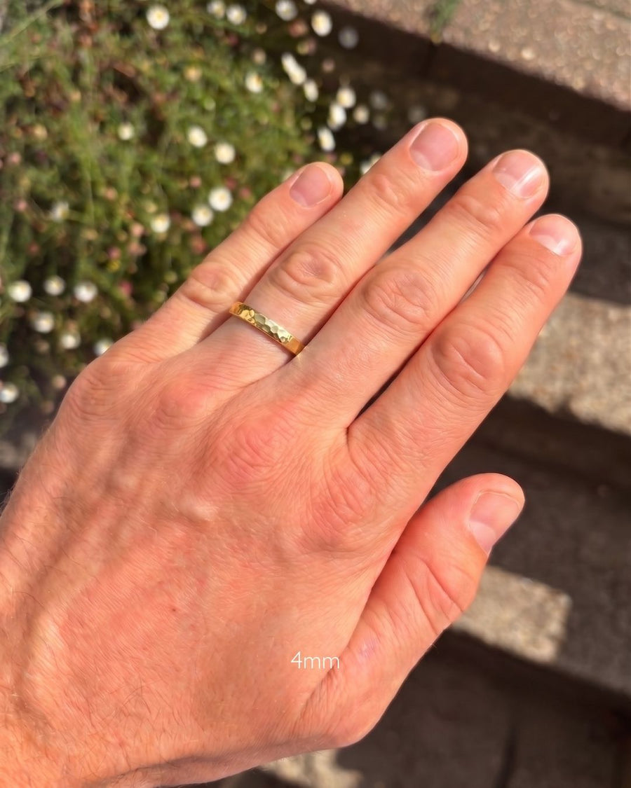 Gold hammered court wedding ring on a man's finger, featuring a 4mm wide band.