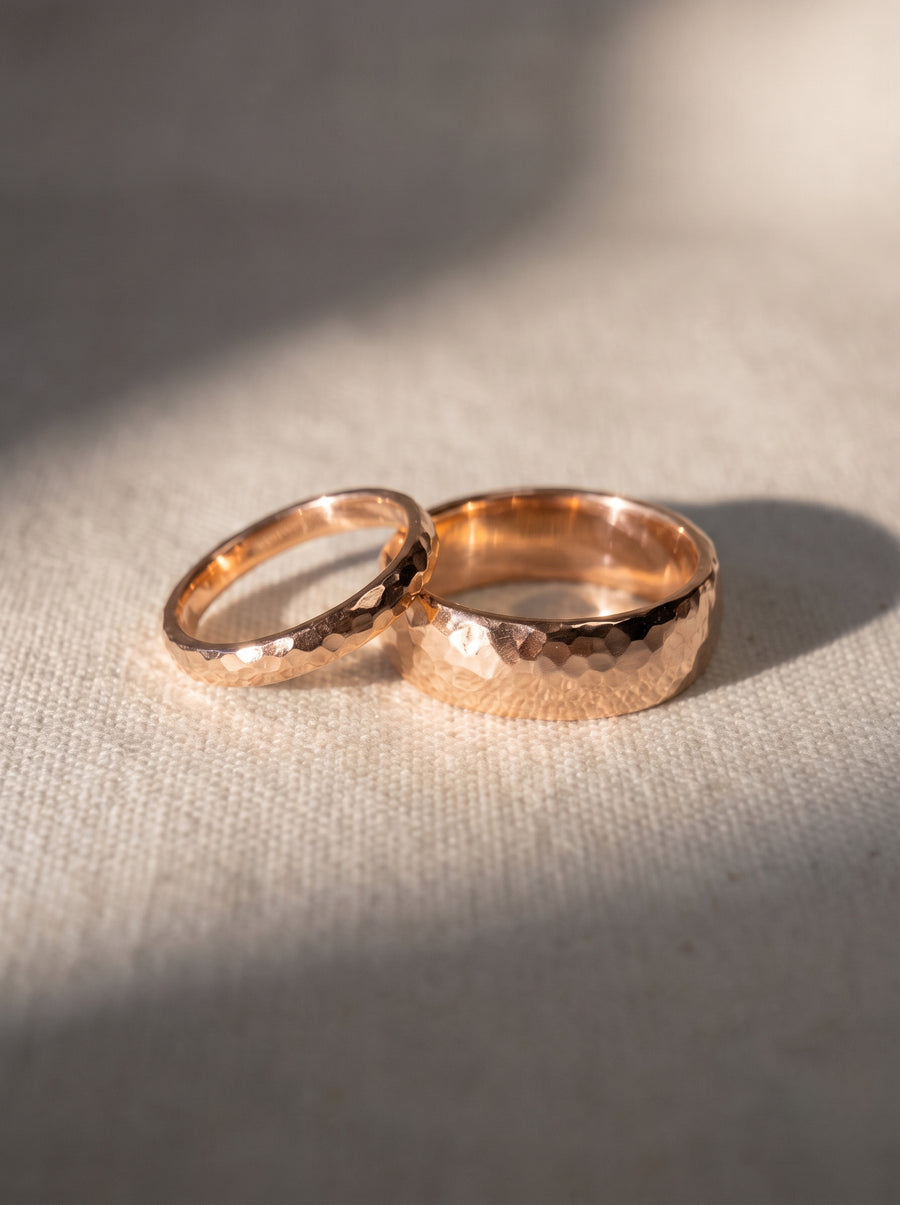 Two 9ct rose gold wedding rings with a hammered texture resting on a textured fabric surface.