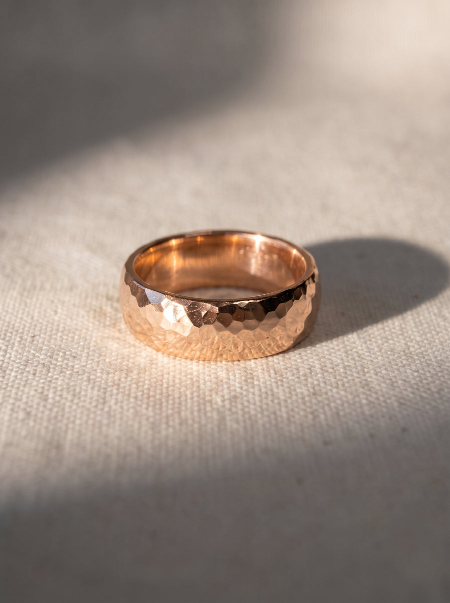 Rose gold wedding ring with a hammered texture and a rounded court profile on a textured fabric surface.