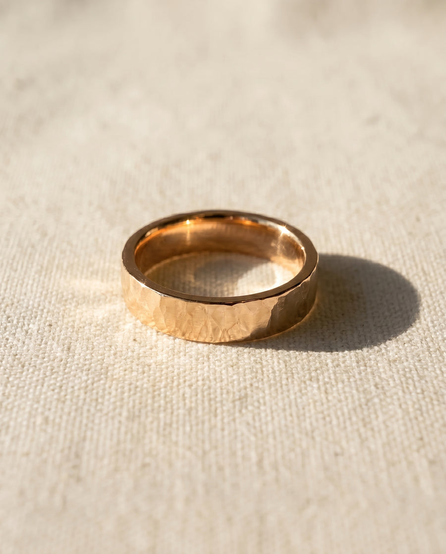 Men's hammered rose gold wedding ring on a light fabric surface.