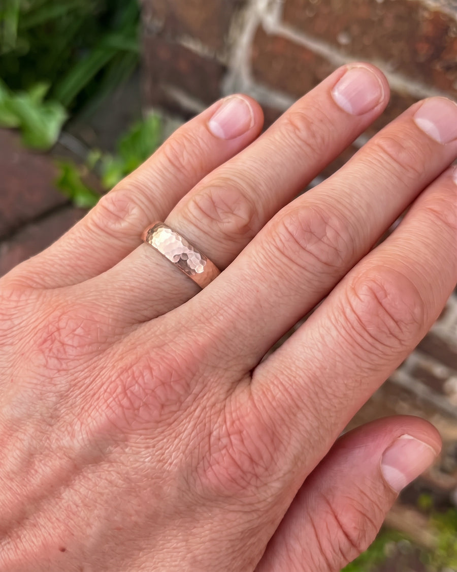 Rose gold court wedding ring with a textured hammered finish worn on a man's finger.