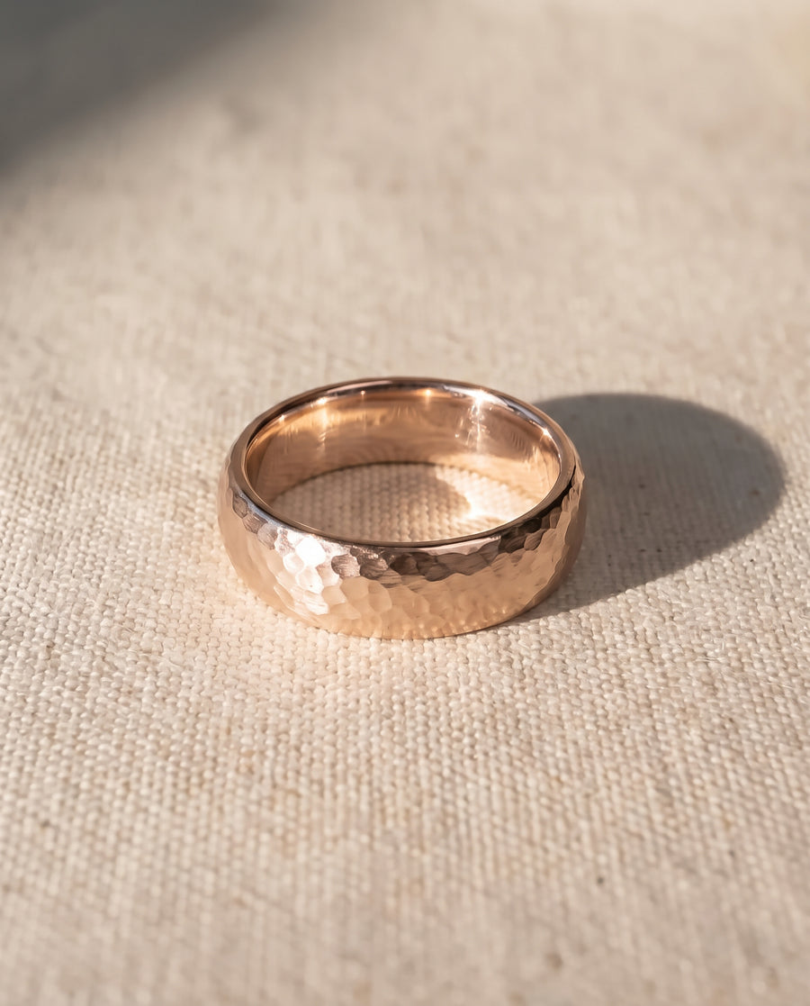 Rose gold wedding ring with a hammered texture on a textured beige fabric surface.