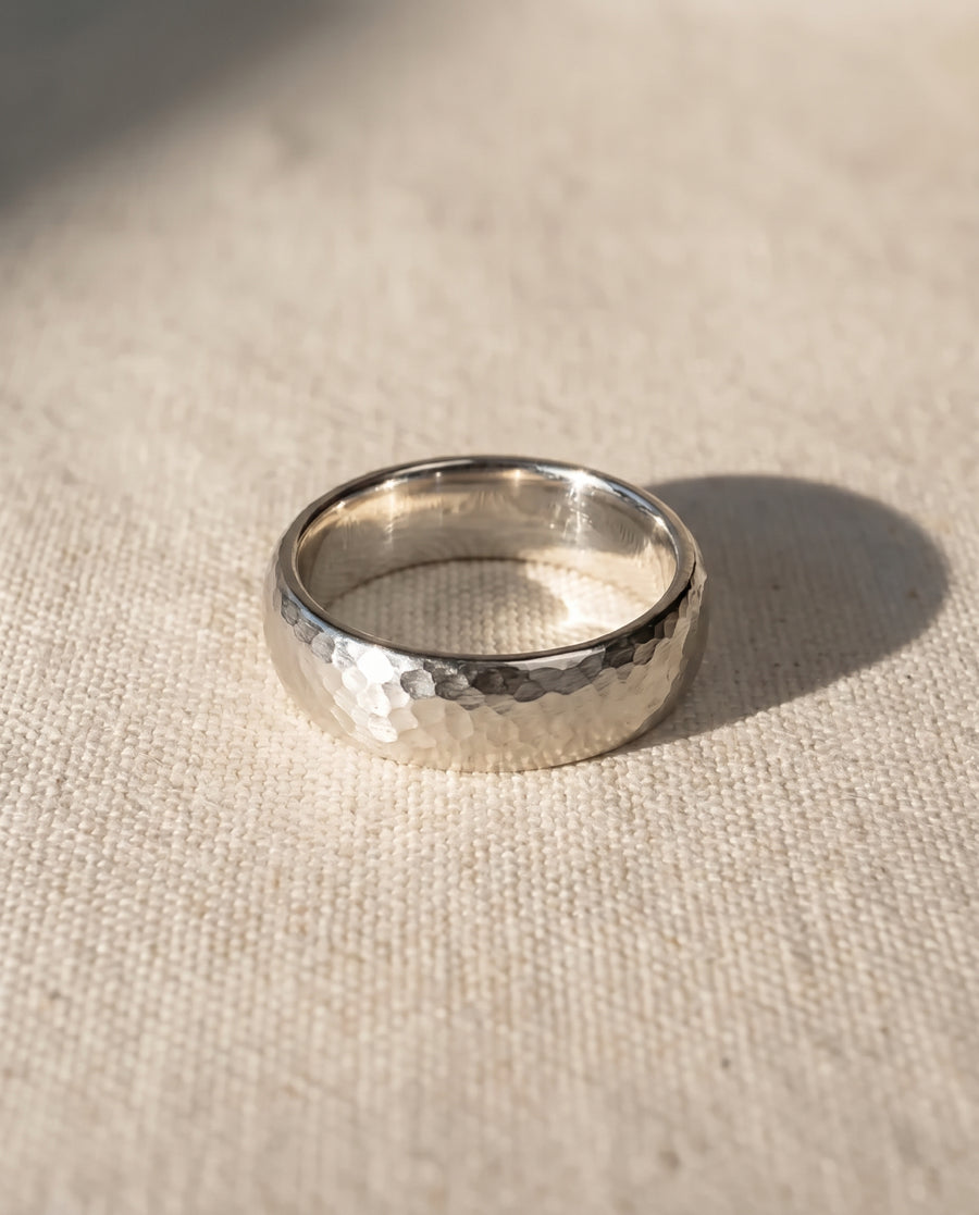 Silver court wedding ring with a textured hammered finish resting on a light fabric surface.