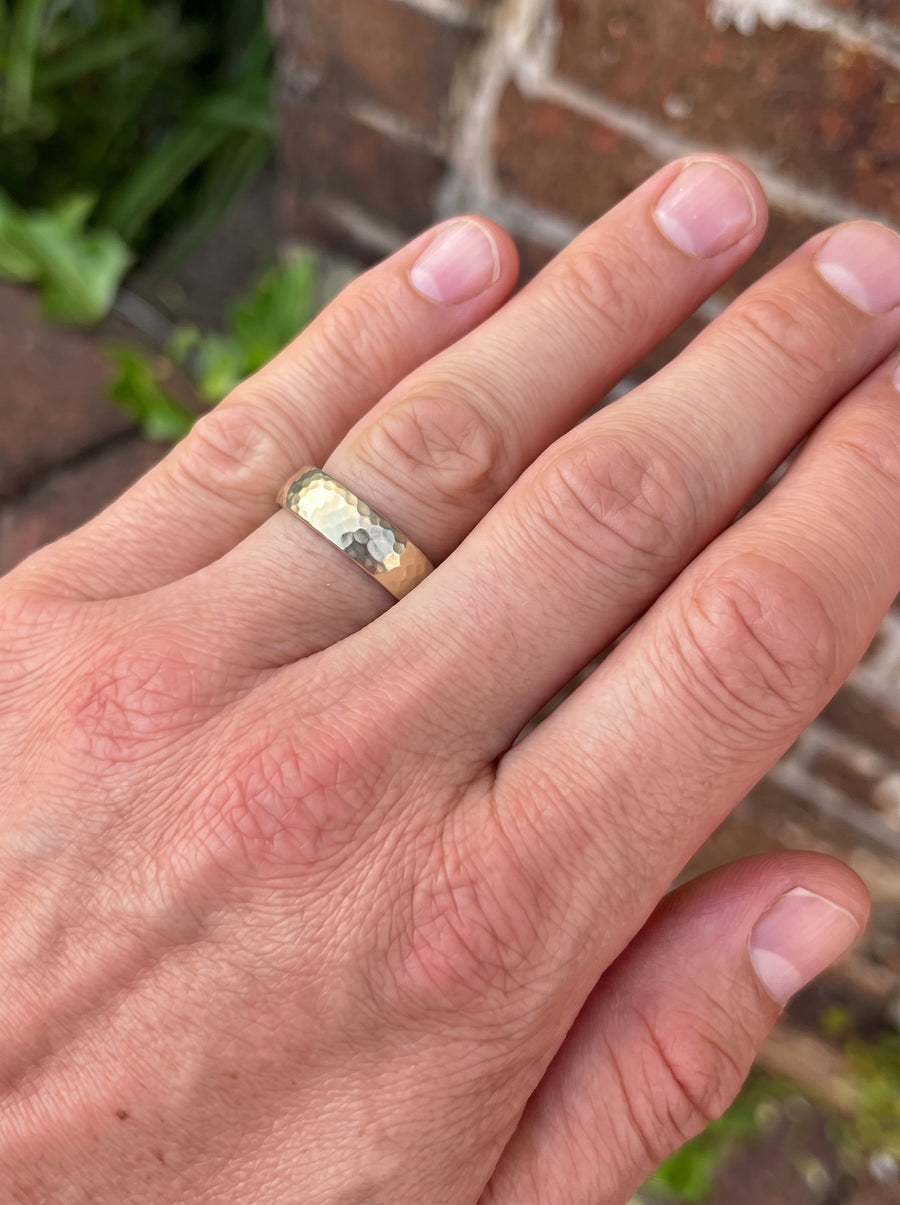 Gold court wedding ring with a hammered texture worn on a finger.