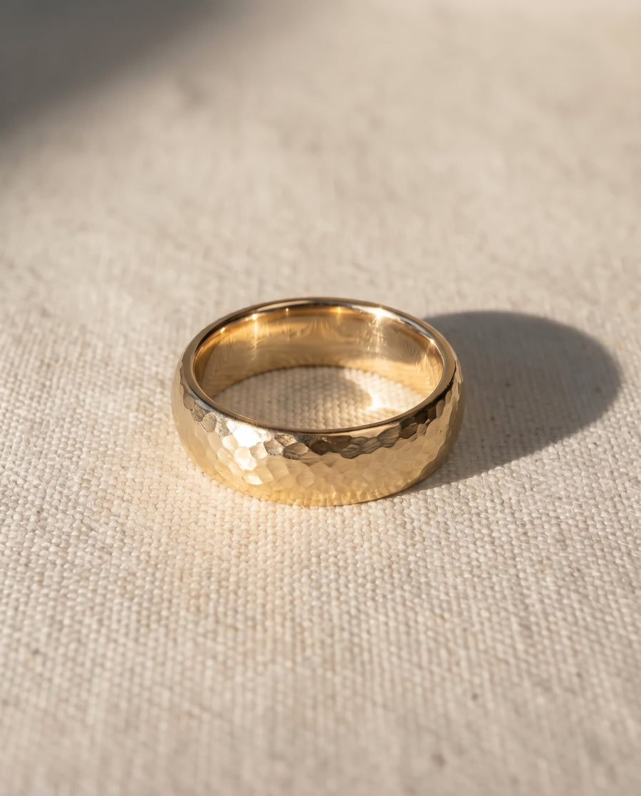 Gold wedding band with a hammered texture and court shape resting on a textured fabric surface.