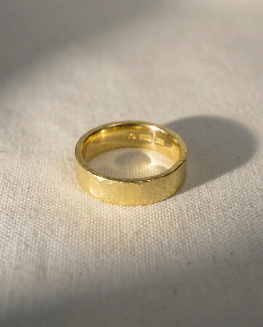9ct yellow gold 4mm hammered wedding ring on a light fabric surface.