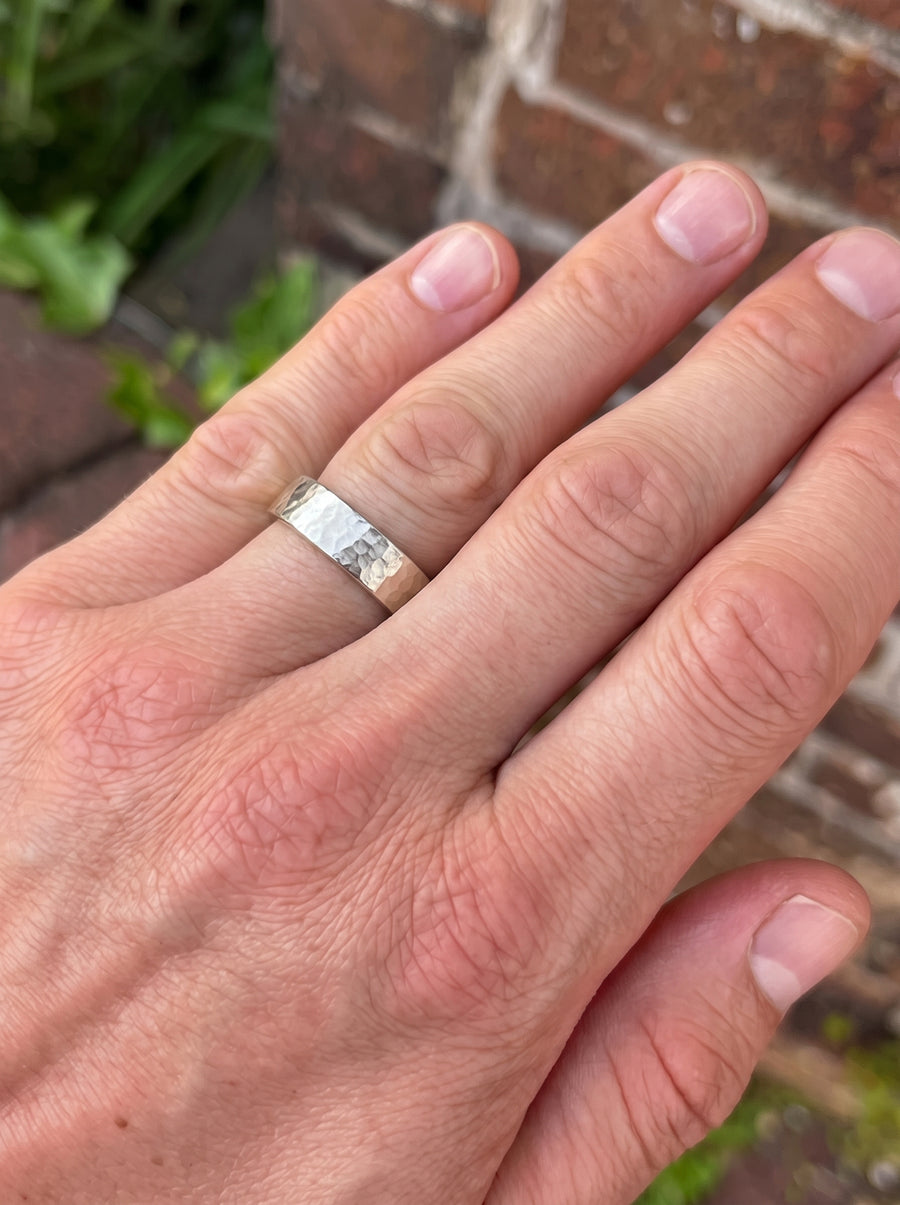 Silver wedding band with a rough hammered texture worn on a man's finger.
