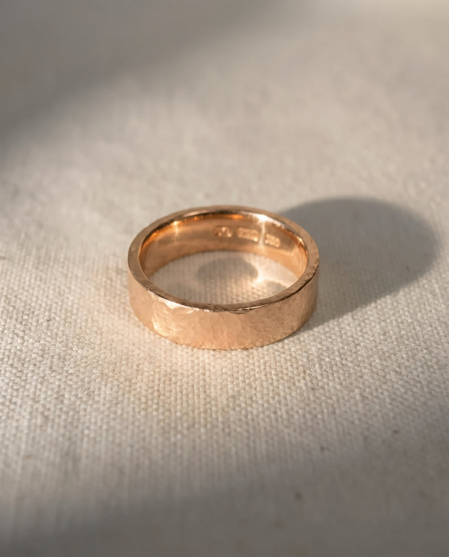4mm wedding ring in 9ct rose gold with a rough hammered texture, resting on a textured fabric surface.