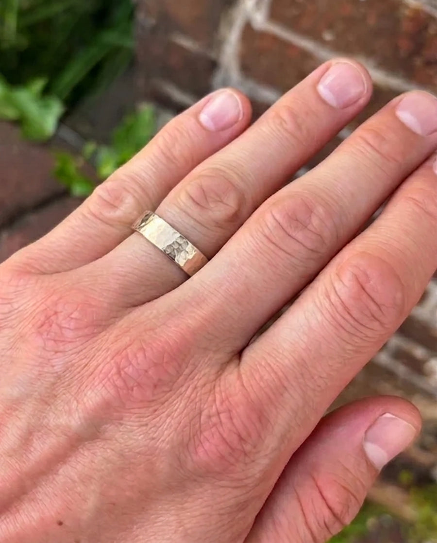 Gold wedding band with a textured, hammered finish worn on a man's finger.